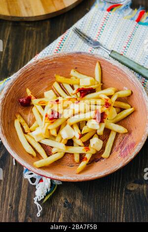 Pommes frites auf schwarzer Oberfläche anprittieren. Kanadisches Gericht mit Kartoffeln, Käse und Sauce Stockfoto