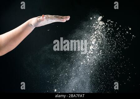 Isoliert auf schwarzem Hintergrund gießt weibliche Hand weißes Mehl wie Schnee zum Backen 2020 Stockfoto