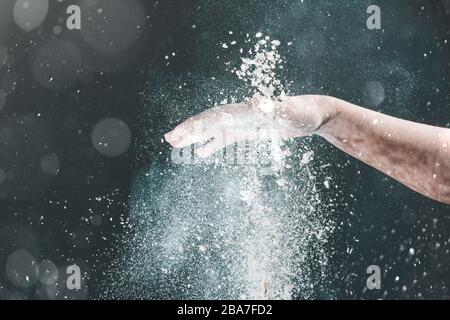 Isoliert auf schwarzem Hintergrund gießt weibliche Hand weißes Mehl wie Schnee zum Backen 2020 Stockfoto