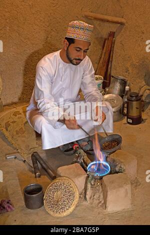 Ein omanischer Mann im traditionellen omanischen Kleid, der Kaffeebohnen auf traditionelle Art und Weise braten lässt. Stockfoto