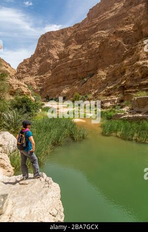 Ein weiblicher Wanderer oder Wanderer, der auf das Wadi Shab im Oman hinunterblickt. Stockfoto