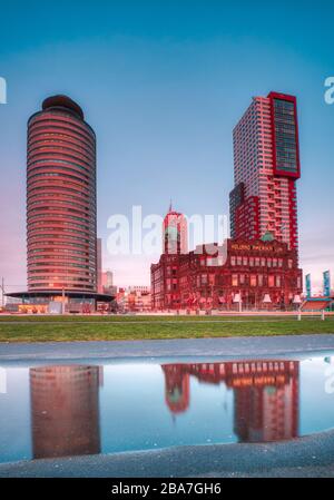 Rotterdam - 12. Februar 2019: Rotterdam, Niederlande. Hotel New York, das Hotel spiegelte sich in der Nacht auf Kop van Zuid auf dem Fußweg im Wasser wider Stockfoto