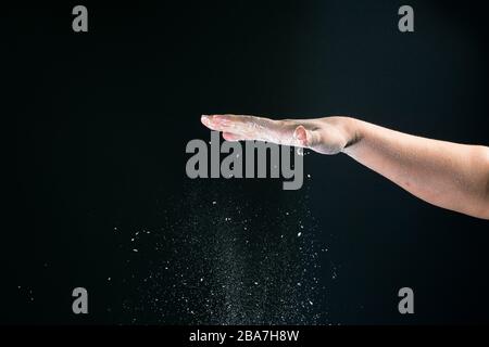 Isoliert auf schwarzem Hintergrund gießt weibliche Hand weißes Mehl wie Schnee zum Backen 2020 Stockfoto