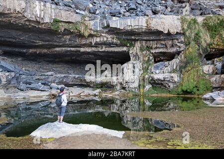 Jebel Shams, Oman. Ein Wasserpool und ein kleiner Wasserfall hoch in den Bergen, in der Nähe der Wanderung, die als Balcony Walk bekannt ist. Ein weiblicher Wanderer sieht auf. Stockfoto