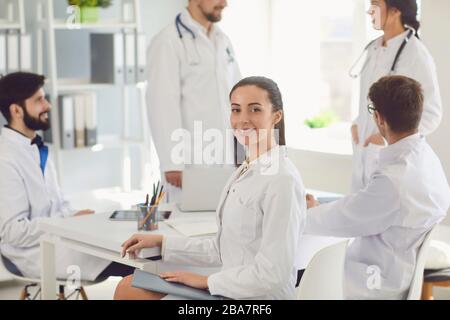 Ärztin sitzt an einem Tisch mit Kollegen in weißen Labormänteln in einem medizinischen Krankenhaus. Stockfoto