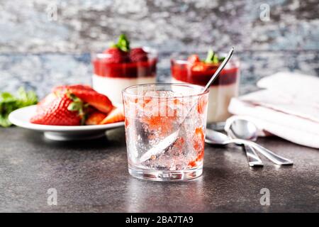 Gegessen wird Panna cotta. Leeren Sie den Glasbecher mit Löffel. Panna Cotta im Hintergrund. Stockfoto