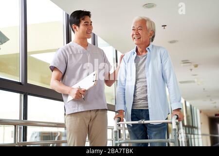 Glückliche ältere asiatische Frau spricht mit körperlichem Therapeuten im Reha-Zentrum Stockfoto
