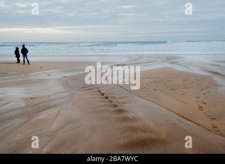 Constantine Bay, ein schöner Sandstrand in der Nähe von Ttevose in Cornwall, an einem herbstlichen Tag mit zwei Menschen, die bei Ebbe die frische Luft spazieren gehen Stockfoto