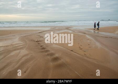 Constantine Bay, ein schöner Sandstrand in der Nähe von Ttevose in Cornwall, an einem herbstlichen Tag mit zwei Leuten, die die frische Luft genießen, die mit einem kleinen Hund spazieren geht Stockfoto