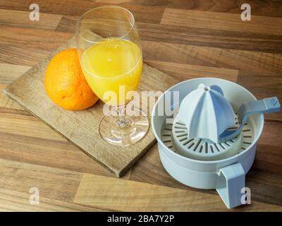 Frisch gepresster Orangensaft mit einer ganzen Orange auf einem Hackbrett und einer Orangenpresse auf einer Holzblockküche Stockfoto