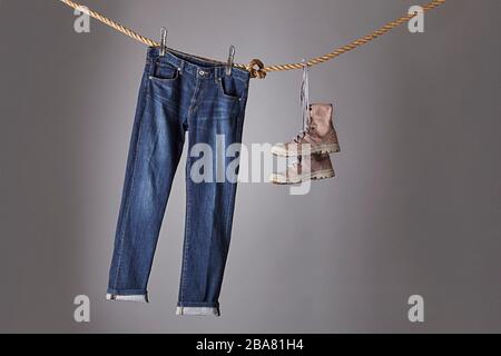 Eine blaue Jeans, die an einem Seil hängt, Seite an Seite mit Stiefeln Stockfoto