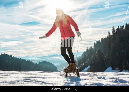 Junge Frau, die mit Vintage-Rodeln auf schneehohem Berg beschleunigt - glückliches Mädchen, das Spaß im Urlaub in der weißen Woche hat - Reisen, Wintersport, Urlaubskonzept Stockfoto