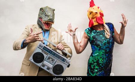 Verrücktes Senioren-Paar tanzt auf Karnevalsparty mit t-rex und Hühnchenmaske - alte Trend-Leute, die Spaß beim Musikhören mit Boombox-Stereo haben - Absu Stockfoto