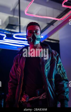 Mixed Race Cyberpunk-Spieler in Maske in der Nähe von Neonbeleuchtung Stockfoto
