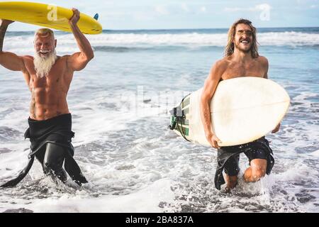 Mehrgenerationige Freunde, die am tropischen Strand surfen - Familienmitglieder haben Spaß am Extremsport - fröhliches älteres und gesundes Lifestyle-Konzept Stockfoto