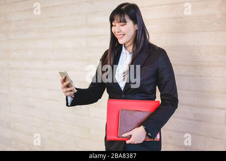 Business asian Woman mit Smartphone-App aus dem Bürogebäude heraus - junge Arbeitsantin - Tech, Unternehmer und Jobkonzept - im Fokus Stockfoto