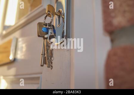 25 Nahaufnahme eines Hausschlüssels im Schlüsselloch einer weißen Tür mit anderen Schlüsseln auf einem Ring, der nach unten hängt Stockfoto