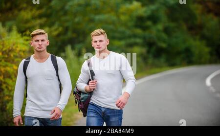 Firmenfreunde Reisende, die auf dem Naturhintergrund der Straße hitchwandern. Beginnen Sie mit dem Wandern ein tolles Abenteuer in Ihrem Leben. Fahren Sie in der Nähe des Stadtrandes. Reisende auf dem Weg. Freunde, die hitchhitchhamps unterwegs Stockfoto