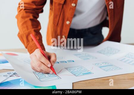 Zugeschnittene Ansicht des ux-Designers mit Markierung für die Entwicklung des Benutzererlebnisdesigns am Tisch, der auf grau isoliert ist Stockfoto