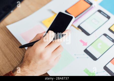 Zugeschnittene Ansicht des ux-Designers mit Smartphone und Stift des Grafiktabletts in der Nähe von mobilen Frameworks auf einem Tisch isoliert auf Schwarz Stockfoto