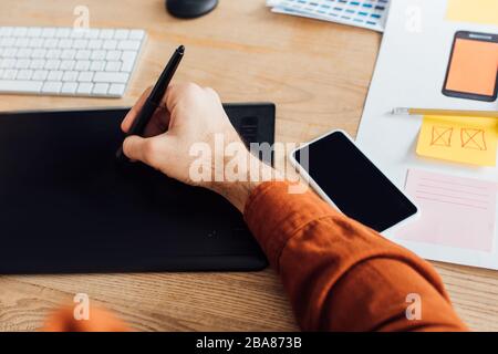Zugeschnittene Ansicht von Entwicklern mit Grafiktablett in der Nähe von Smartphones und Vorlagen für mobiles ux-Design auf dem Tisch Stockfoto
