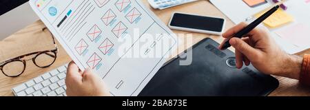 Zugeschnittene Ansicht des Designers mit Grafiktablett bei der Planung des Benutzererlebnisses Gestaltung der Website am Tisch, Panoramaaufnahme Stockfoto