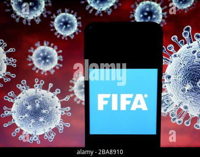 In dieser Abbildung wird ein Logo der Fédération Internationale de Football Association (FIFA) auf einem Smartphone mit einem Computermodell des COVID-19-Coronavirus als Hintergrund angezeigt. Stockfoto