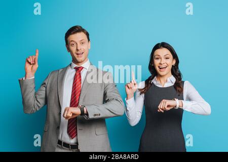 Zwei lächelnde Geschäftsleute zeigen Ideenschilder, während sie die Kamera auf blauem Hintergrund betrachten Stockfoto