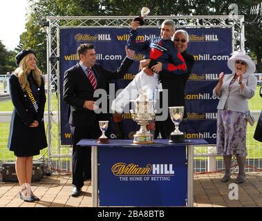 Paul Mulrennan der Jockey von Mass Rally der Gewinner des William Hill Ayr Silver Cup wird vom Besitzer Martin Pearson angehoben, während sie mit der Trophäe feiern Stockfoto