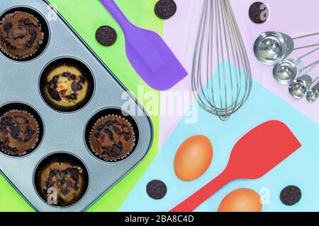 Blick auf frische hausgemachte Vanila-, Kaffee- und Schokoladenmuffins in Papierkuchenhalter mit Plätzchen und Creme, isoliert auf farbenfrohem Backgrou Stockfoto