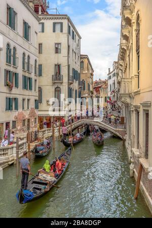 Venedig, Venetien, Italien 24. Juli 2017 Gondeln mit Passagieren, die einem belebten Kanal im Zentrum venedigs folgen Stockfoto