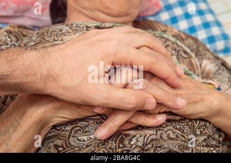 Mann, der die Hände seiner Oma berührt. Unterstützende Haltung, das Liebeskonzept zeigt. Stockfoto