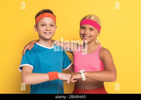 Lächelnde Kinder in Sportswear umarmen sich und tun Faustschlag auf gelbem Hintergrund Stockfoto