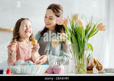 Selektive Konzentration von Tulpen in der Nähe von Hühnereiern, osterbrot, glücklicher Mutter und Tochter Stockfoto