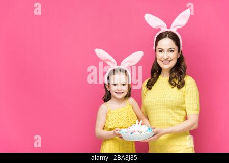 Glückliche Mutter und Tochter in Hünenähren, die Ostereier auf Rosa abhielten Stockfoto