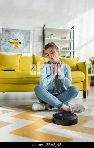 Junge Frau, die im Wohnzimmer einen Roboter-Staubsauger auf dem Teppich betrachtet Stockfoto