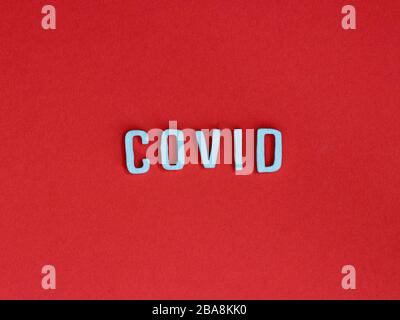 Covid mit Holzbuchstaben geschrieben, die auf rotem Hintergrund isoliert sind Stockfoto