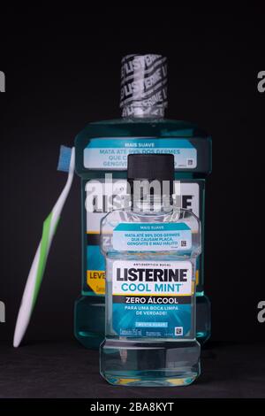Große Flasche Mundspülung mit einer Zahnbürste zur Seite, um die Waage mit kleinen im Vorderteil zu zeigen. Niedrige Schlüsselaufnahme von Mundhygieneprodukten vor dunklem Hintergrund. Stockfoto