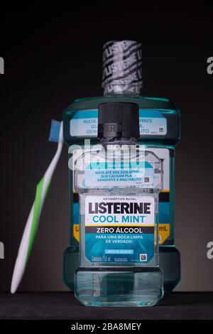 Große Flasche Mundspülung mit einer Zahnbürste zur Seite, um die Waage mit kleinen im Vorderteil zu zeigen. Niedrige Schlüsselaufnahme von Mundhygieneprodukten vor dunklem Hintergrund. Stockfoto