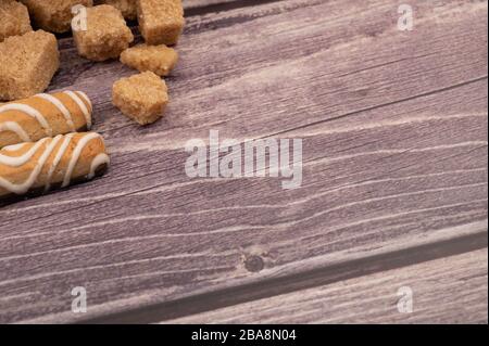 Stücke von braunem Rohrzucker und Plätzchenstäbchen mit Schokolade und weißer Vereisung auf Holzhintergrund. Nahaufnahme Stockfoto