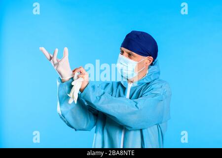 Mann in einem weißen Dekontaminationsanzug, der medizinische Handschuhe anlegt Stockfoto