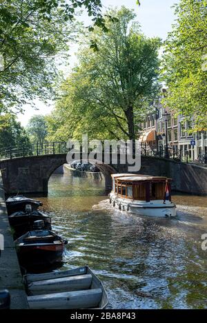 Ein Kanalboot nähert sich einer Brücke in Amsterdam, Nordholland, Niederlande Stockfoto