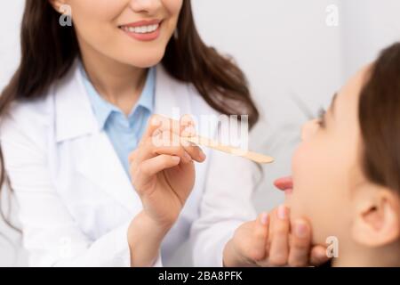 Beschnittener Blick auf einen enthohlenen Arzt, der die Kehle des Kindes mit Zungenentpresser untersucht Stockfoto