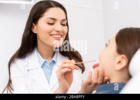 Selektiver Fokus des lächelnden Otolaryngologen, der die Kehle des Kindes mit Zungenentpresser untersucht Stockfoto