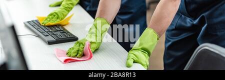 Teilweise Ansicht der Reiniger in Gummihandschuhen Reinigung Büroschreibtisch und Computertastatur Stockfoto