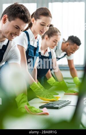 Selektiver Fokus der jungen multikulturellen Reiniger, die Schreibtische mit Lappen im Büro reinigen Stockfoto