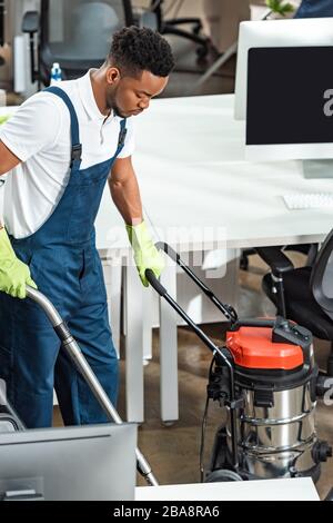 Junger afroamerikanischer Reinigungsboden im Büro mit Staubsauger Stockfoto