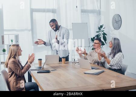 Lächelnde multikulturelle Kollegen klatschen während des Treffens in der Kreativagentur Stockfoto