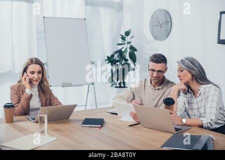 Lächelnde multikulturelle Kollegen, die in der Kreativagentur mit Gadgets sprechen und arbeiten Stockfoto