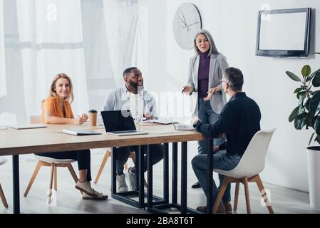 Lächelnde multikulturelle Kollegen, die mit asiatischen Geschäftsfrauen sprechen Stockfoto